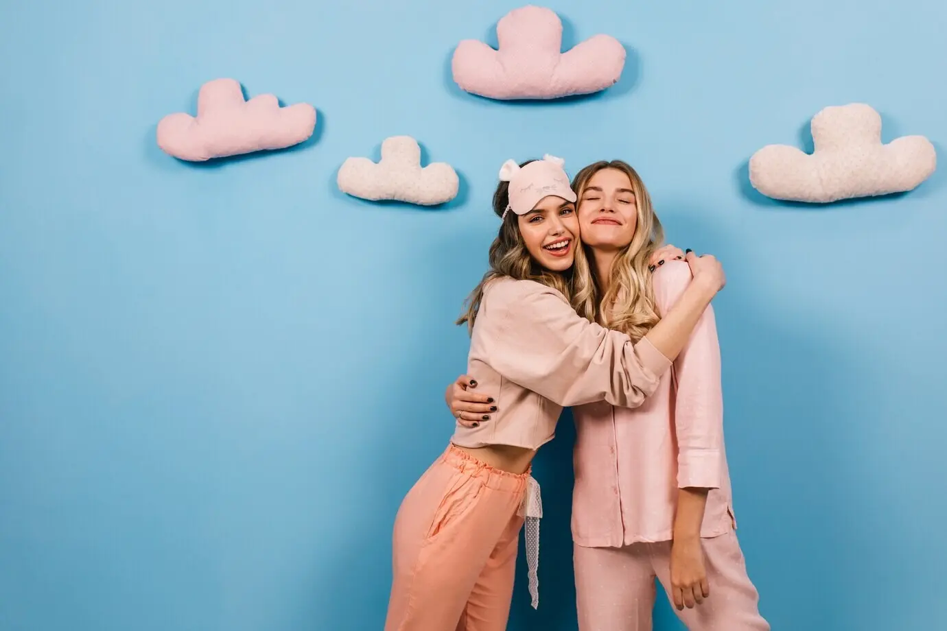 Bezaubernde Frauen umarmen sich vor einer blauen Wand mit Wolken.