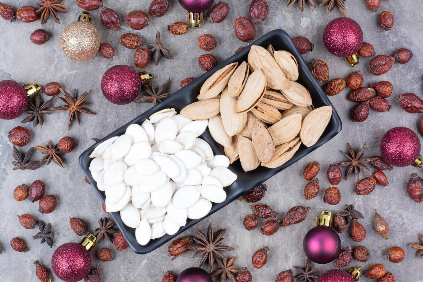 Schale mit Pistazien- und Kürbiskernen sowie Hagebutten und Weihnachtskugeln.